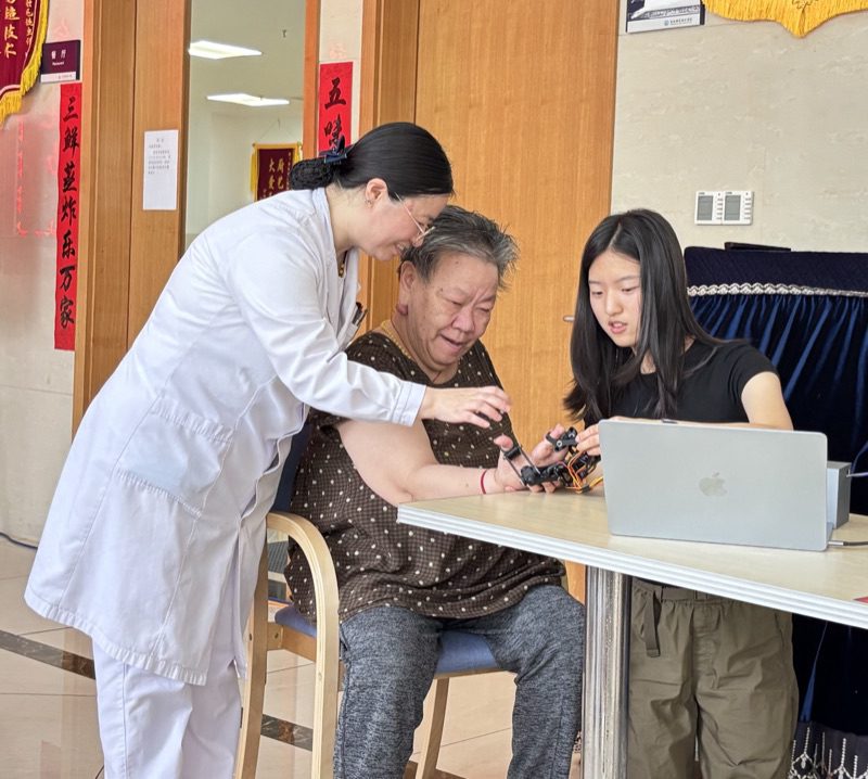 A clinician steadies a resident's arm while she tries the device, Yanzi at the laptop