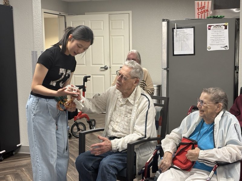 Yanzi helping a seated resident use the device while other residents look on