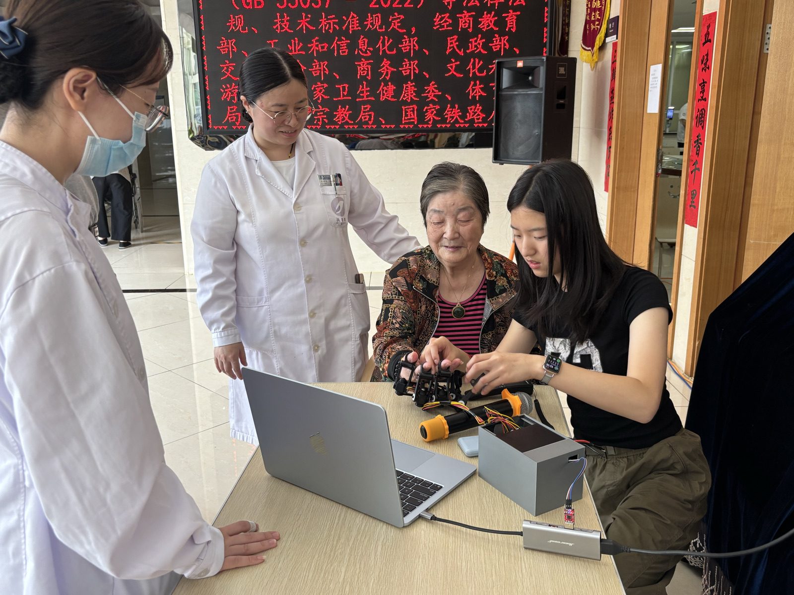 Two clinicians in white coats watch as a resident tries the device with Yanzi at a laptop