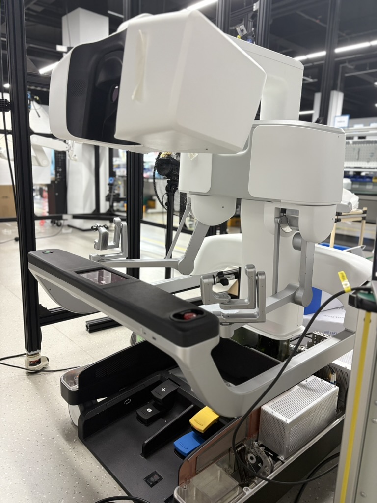 Side view of a surgeon console showing the viewing unit, hand controls, and foot pedals